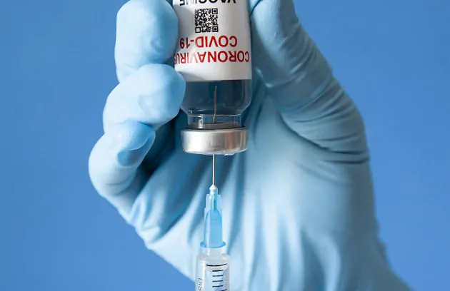 A technician uses a third dose of a COVID-19 vaccine