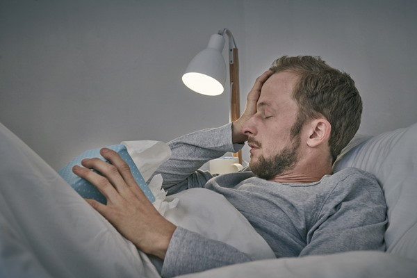 In the color photo, a man is lying on a bed with his hands on his head.