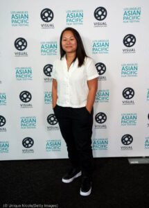 Asian woman poses for a photo in casual attire.  In the background, festival ads (© Unique Nicole / Getty Images)